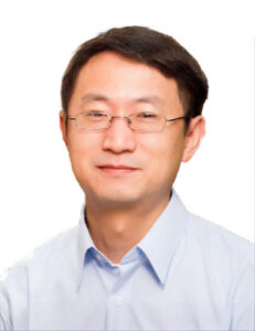 A man with short dark hair and glasses, wearing a light blue collared shirt, poses against a plain white background.